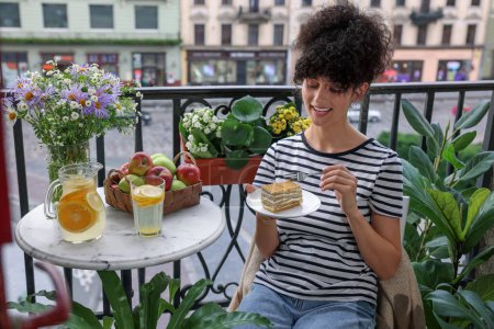 Téléchargez les photos : Jeune femme manger morceau de gâteau sur le balcon avec de belles plantes d'intérieur - en image libre de droit