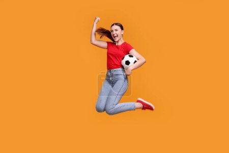 Photo for Emotional soccer fan with ball jumping on orange background - Royalty Free Image