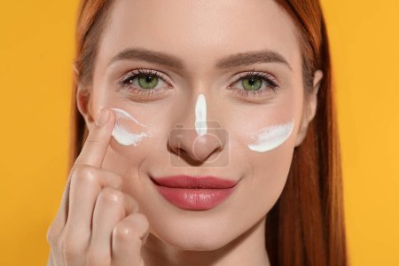 Photo for Beautiful young woman with sun protection cream on her face against orange background, closeup - Royalty Free Image