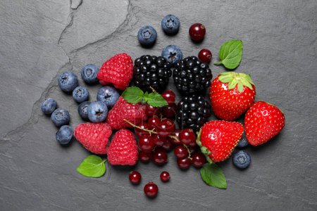 Photo for Many different fresh ripe berries and green leaves on dark grey table, flat lay - Royalty Free Image