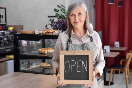 Smiling business owner holding open sign in her cafe, space for text