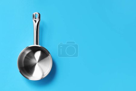 Empty steel saucepan on light blue background, top view. Space for text