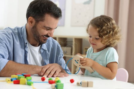 Motorische Entwicklung. Vater und Tochter spielen mit Holzschnürspielzeug am Tisch im Haus