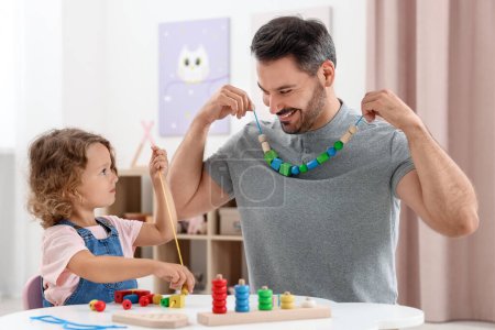 Développement des compétences motrices. Père et fille jouant avec des pièces en bois et de la ficelle pour l'activité de filetage à la table à l'intérieur