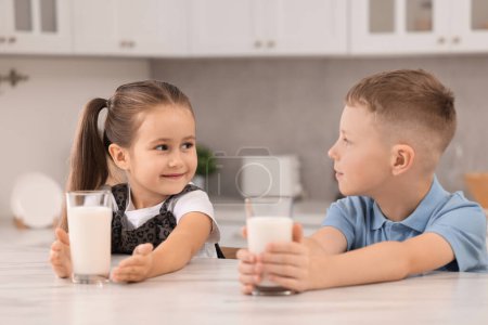 Téléchargez les photos : Enfants mignons avec des verres de lait à la table blanche dans la cuisine - en image libre de droit