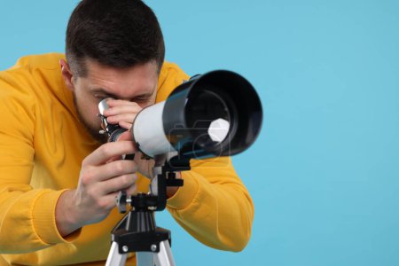 Astronomer looking at stars through telescope on light blue background. Space for text