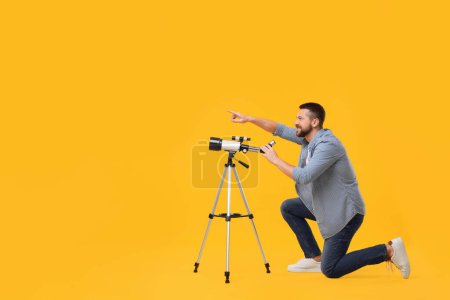 Happy astronomer with telescope pointing at something on orange background. Space for text