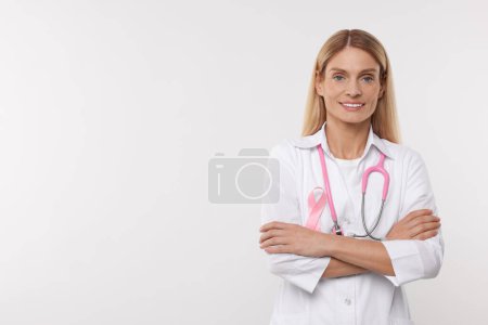 Doctor with pink ribbon and stethoscope on white background, space for text. Breast cancer awareness