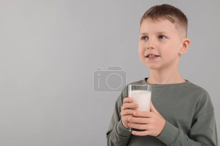 Téléchargez les photos : Mignon garçon avec verre de lait frais sur fond gris clair, espace pour le texte - en image libre de droit