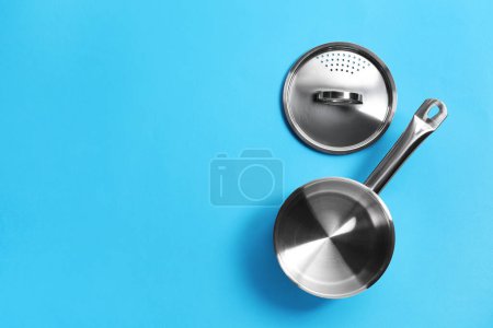 Empty steel saucepan and strainer lid on light blue background, flat lay. Space for text