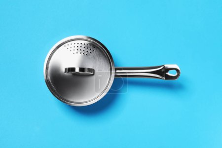 Photo for Steel saucepan with strainer lid on light blue background, top view - Royalty Free Image