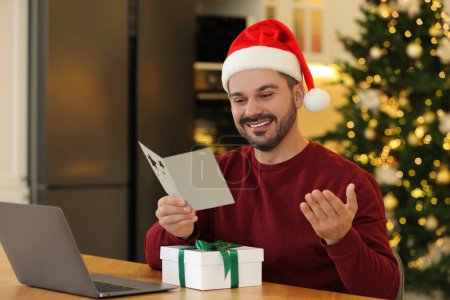 Weihnachten online feiern und Geschenke per Post austauschen. Mann liest Grußkarte während Videoanruf auf Laptop zu Hause