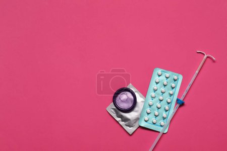 Contraception choice. Pills, condoms and intrauterine device on magenta background, flat lay. Space for text