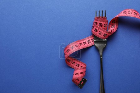 Fork with measuring tape on blue background, top view and space for text. Diet concept
