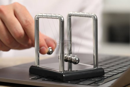 Man playing with Newton's cradle and laptop on table, closeup. Physics law of energy conservation