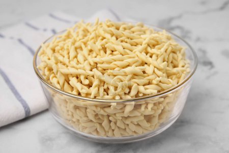 Uncooked trofie pasta in bowl on white marble table, closeup