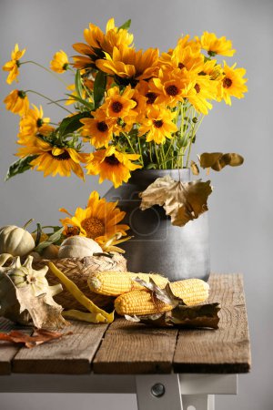Beautiful autumn bouquet, small pumpkins and corn cobs on wooden table against grey background