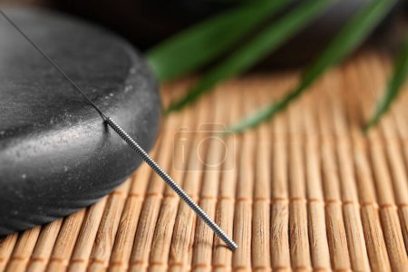 Aguja de acupuntura y piedra spa en estera de bambú, primer plano. Espacio para texto
