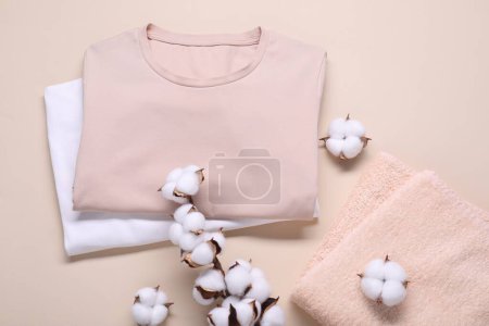 Baumwollzweig mit flauschigen Blumen, T-Shirts und Frottee auf beigem Hintergrund, flache Lage