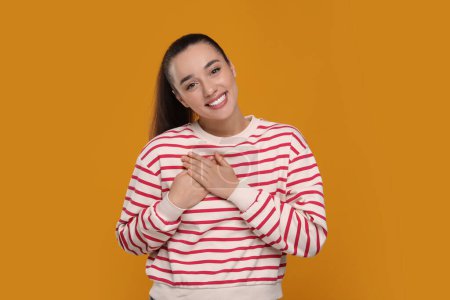 Thank you gesture. Beautiful grateful woman with hands on chest against orange background