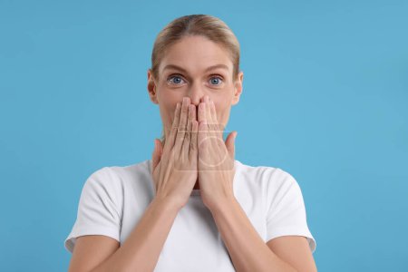 Portrait of embarrassed woman covering mouth with hands on light blue background