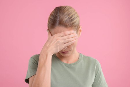Embarrassed woman covering eyes on pink background