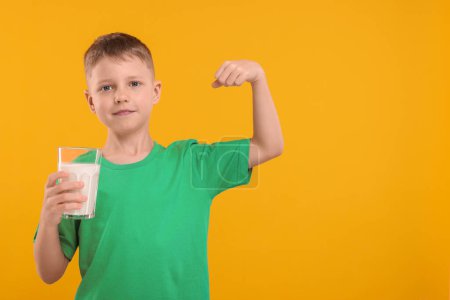 Téléchargez les photos : Garçon mignon avec verre de lait frais montrant sa force sur fond orange, espace pour le texte - en image libre de droit