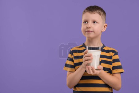 Téléchargez les photos : Garçon mignon avec verre de lait frais sur fond violet, espace pour le texte - en image libre de droit