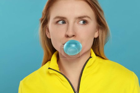 Beautiful young woman blowing bubble gum on light blue background