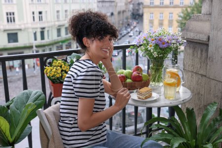 Téléchargez les photos : Jeune femme manger morceau de gâteau à table sur le balcon avec de belles plantes d'intérieur - en image libre de droit