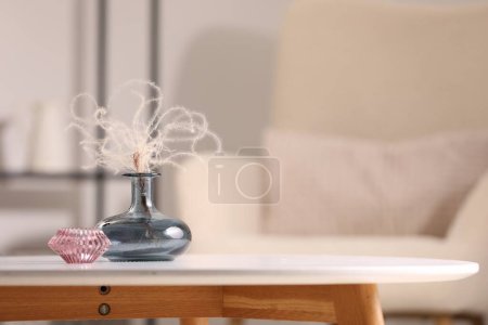 Vase with dried plant and candle on white table in living room, space for text