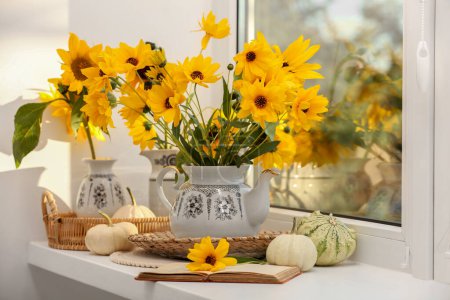 Composition with beautiful flowers, pumpkins and book on windowsill. Autumn atmosphere