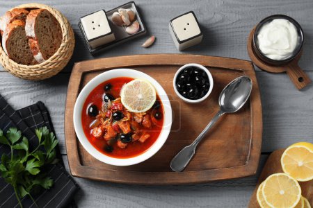 Fleischsoljanka-Suppe mit Würstchen, Oliven und Gemüse auf grauem Holztisch serviert, flach gelegt