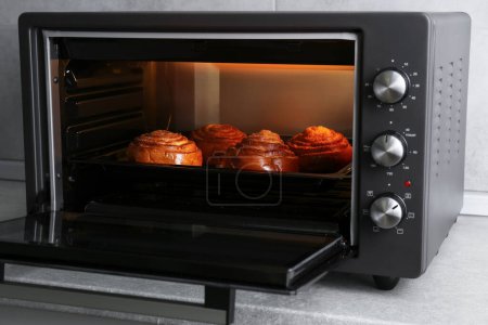 Open electric oven with delicious pastry on grey table indoors