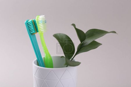 Téléchargez les photos : Brosses à dents et brindilles en plastique coloré dans un récipient sur fond clair, gros plan - en image libre de droit