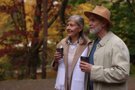 Téléchargez les photos : Couple sénior affectueux avec tasses de café dans le parc d'automne, espace pour le texte - en image libre de droit