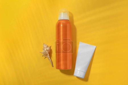 Sunscreens and seashell on yellow background, flat lay. Sun protection care