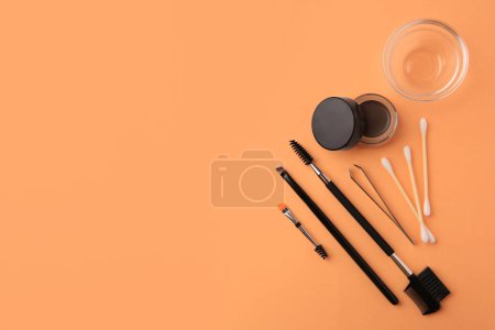 Pommade à sourcils avec effet henné et outils professionnels sur fond orange, pose plate. Espace pour le texte