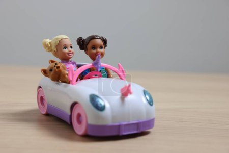 Leyde, Pays-Bas - 20 septembre 2023 : Belles poupées Chelsea avec animal de compagnie dans une voiture jouet sur une table en bois sur fond gris clair, espace pour le texte