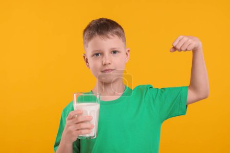 Téléchargez les photos : Mignon garçon avec un verre de lait frais montrant sa force sur fond orange - en image libre de droit