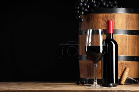 Photo for Delicious wine, wooden barrel and ripe grapes on table against black background. Space for text - Royalty Free Image