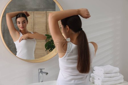 Beautiful young woman doing breast self-examination near mirror in bathroom