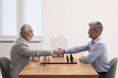 Hombres estrechando sus manos durante el torneo de ajedrez en la mesa en el interior