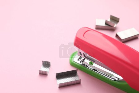Bright stapler with staples on pink background, space for text