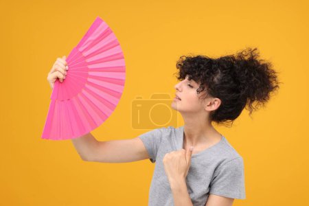 Foto de Mujer con abanico de mano sufriendo de calor sobre fondo naranja - Imagen libre de derechos