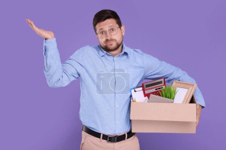 Téléchargez les photos : Chômeur avec boîte d'effets personnels de bureau sur fond violet - en image libre de droit