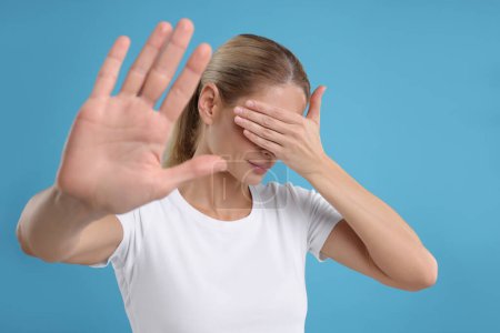 Embarrassed woman covering face on light blue background