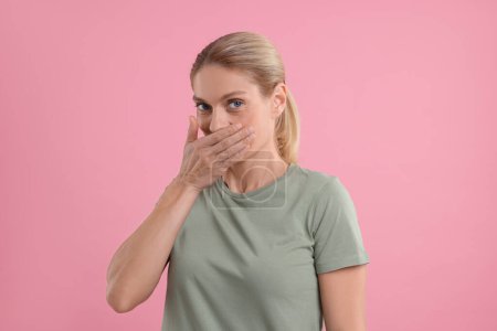 Retrato de mujer avergonzada cubriendo la boca con la mano sobre fondo rosa