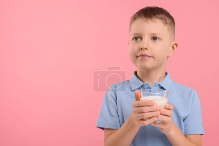 Téléchargez les photos : Garçon mignon avec verre de lait frais sur fond rose, espace pour le texte - en image libre de droit
