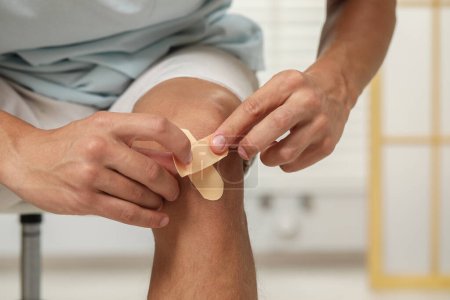 Photo for Man putting sticking plasters onto knee indoors, closeup - Royalty Free Image